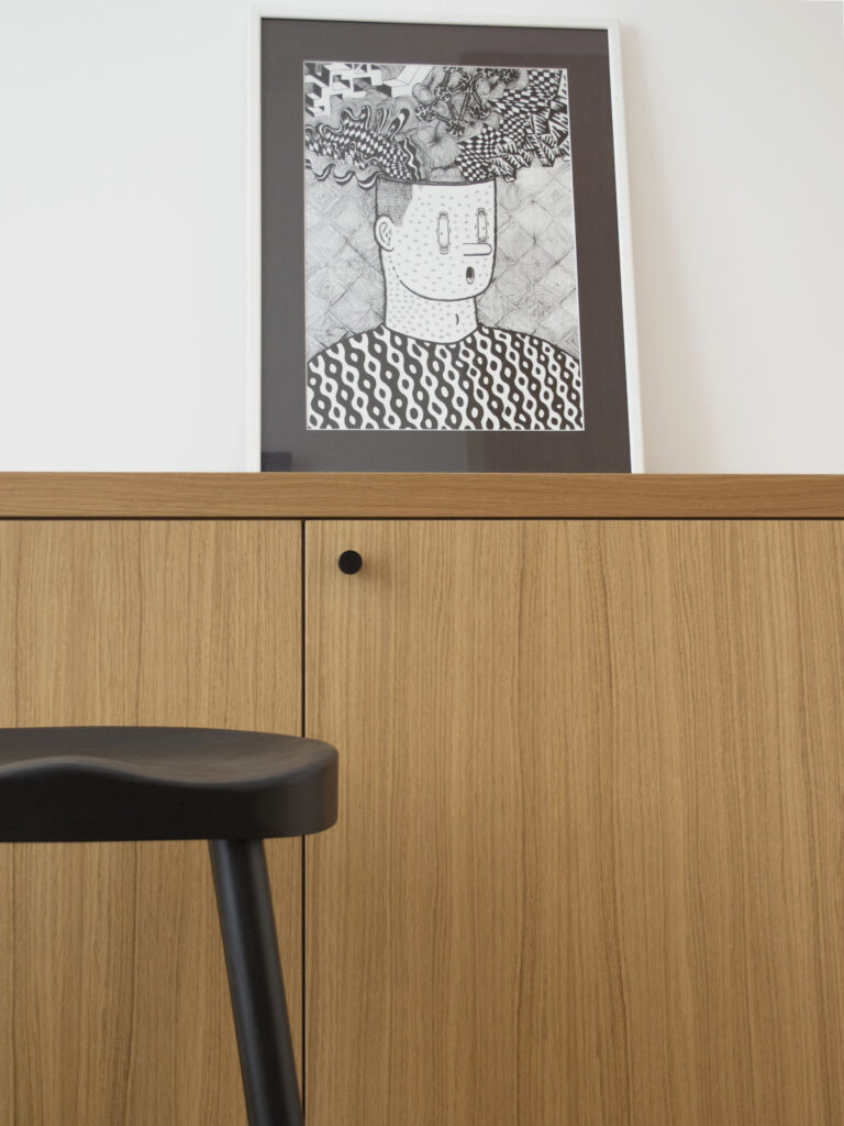 Umetnička ilustracija iznad komode od svetlog drveta u savremenom enterijeru